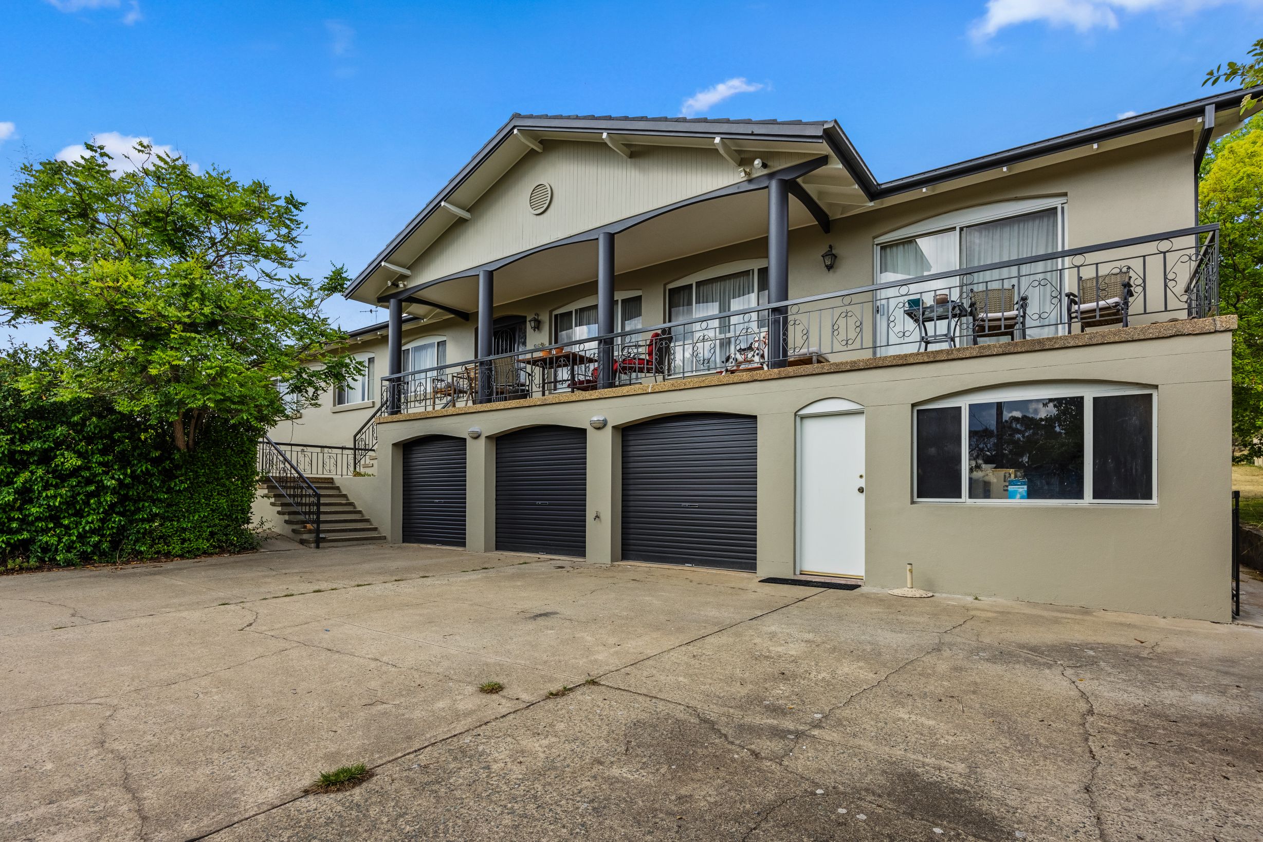 Residential home exterior in Queanbeyan featuring a fresh paint job, balcony with seating, and three garage doors, showcasing the transformation by C&C Painting Group.