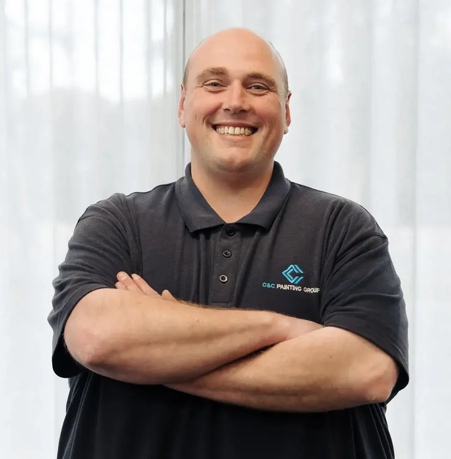 Matthew Chamberlain, lead estimator at C&C Painting Group, smiling with arms crossed, wearing a branded polo shirt, in a well-lit indoor setting.