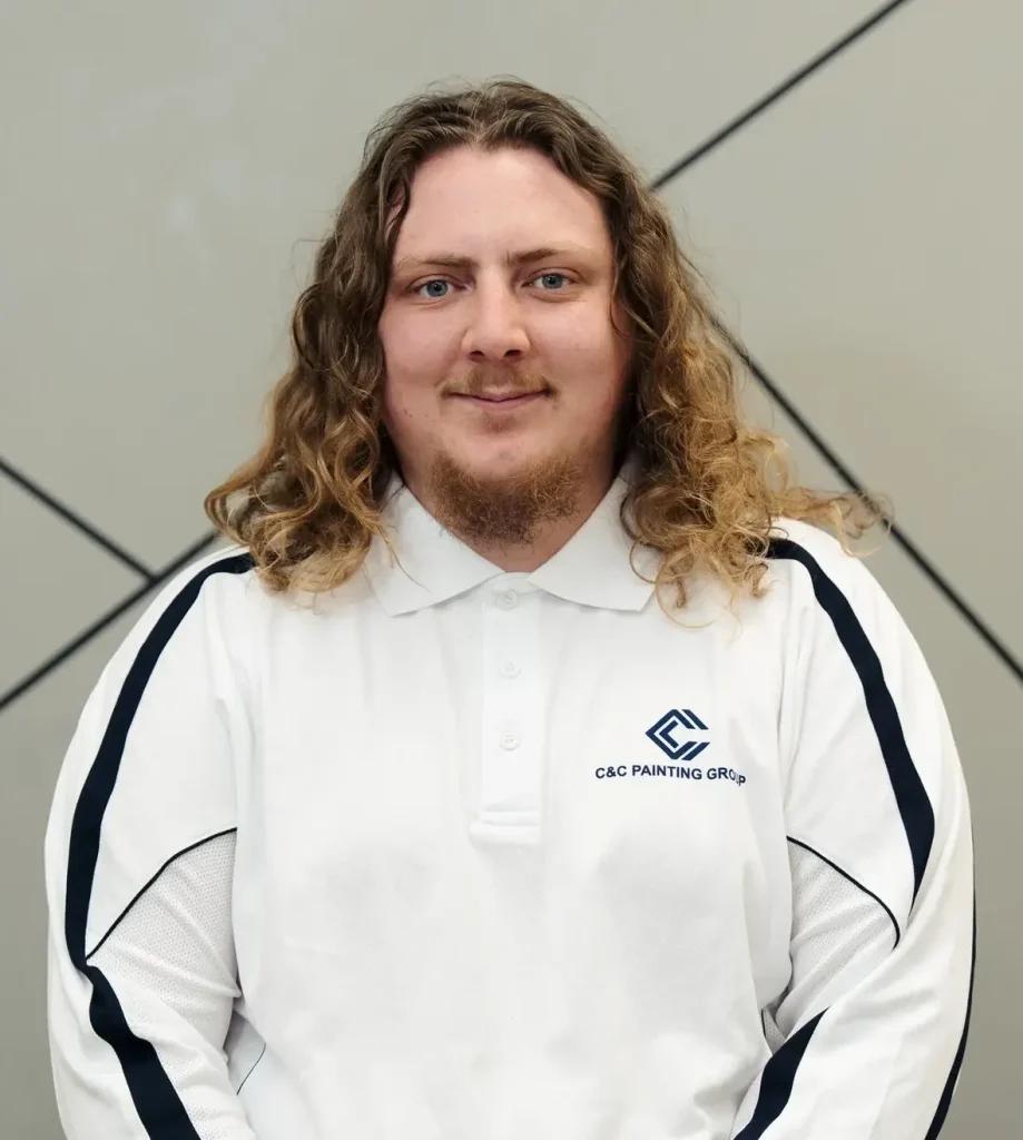 Bradley Logan, painter and team leader at C&C Painting Group, wearing a branded white polo shirt, smiling against a geometric background.