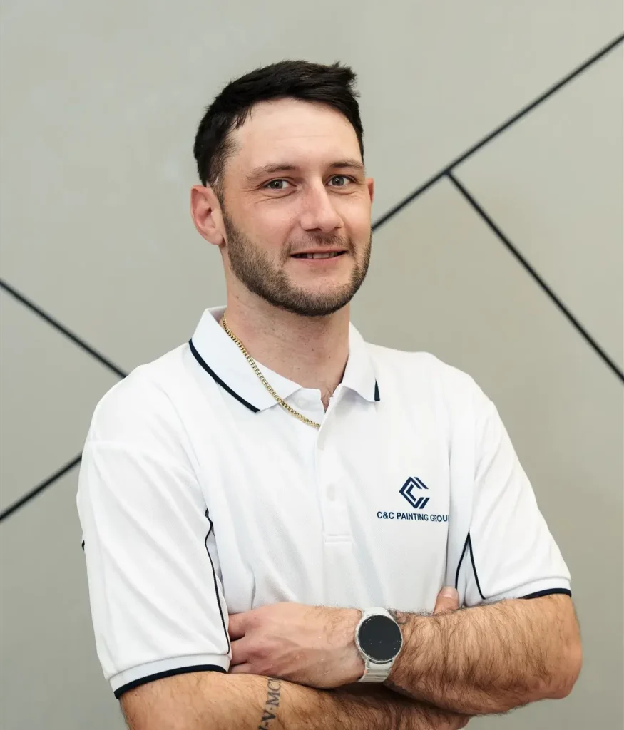 Mitchell Bucholtz, painter and team leader at C&C Painting Group, smiling with arms crossed, wearing a branded polo shirt, showcasing professionalism and expertise in painting services.