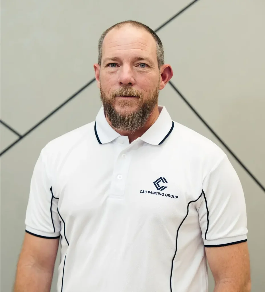 Mathew Cook, Team Leader at C&C Painting Group, wearing a branded polo shirt, standing against a modern geometric background, showcasing his expertise in painting and decorating.